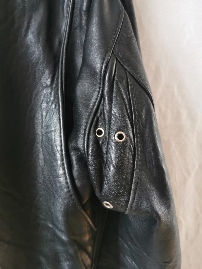 K&ouml;nnte beinhalten: Schwarze Lederjacke mit Rei&szlig;verschluss und zwei silbernen &Ouml;sen am &Auml;rmel.