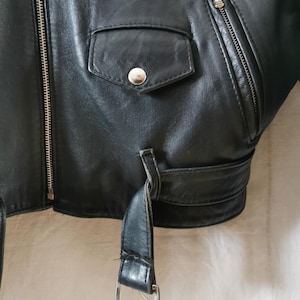 K&ouml;nnte beinhalten: Schwarze Lederjacke mit Rei&szlig;verschluss, einer Druckknopftasche und einem G&uuml;rtel mit einer silbernen Schnalle.