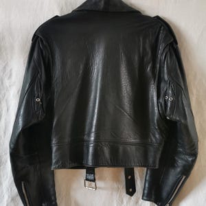 K&ouml;nnte beinhalten: Schwarze Lederjacke im Motorrad-Stil mit Rei&szlig;verschluss, zwei Taschen und einem G&uuml;rtel an der Taille.