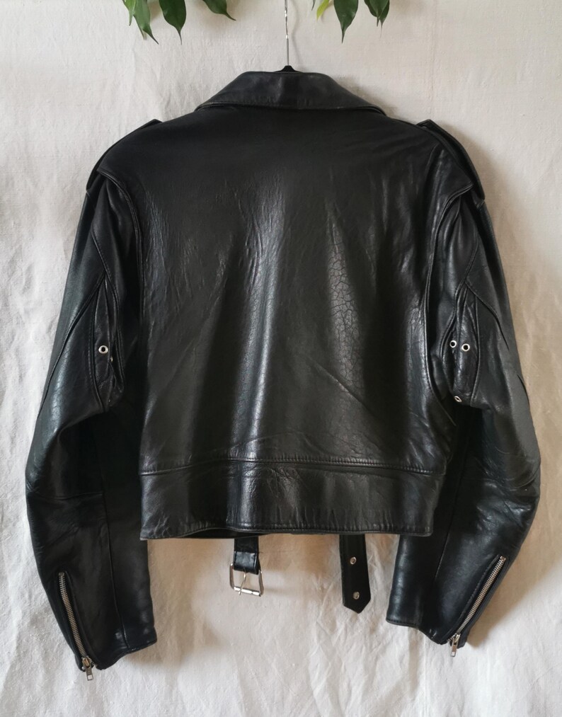 K&ouml;nnte beinhalten: Schwarze Lederjacke im Motorrad-Stil mit Rei&szlig;verschluss, zwei Taschen und einem G&uuml;rtel an der Taille.