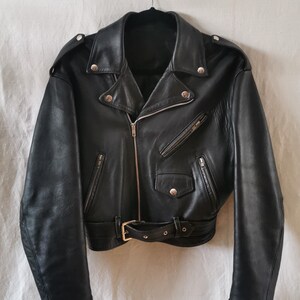 K&ouml;nnte beinhalten: Eine schwarze Lederjacke mit Rei&szlig;verschluss, G&uuml;rtel und mehreren Taschen.
