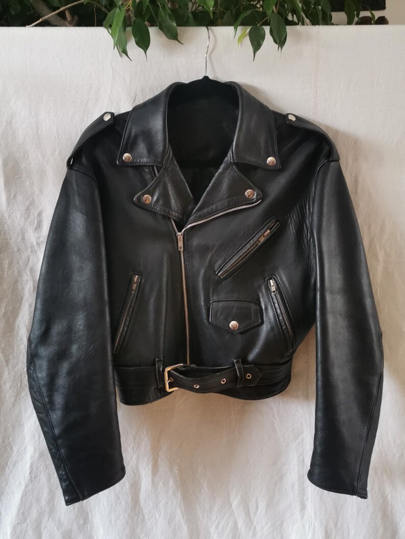 K&ouml;nnte beinhalten: Eine schwarze Lederjacke mit Rei&szlig;verschluss, G&uuml;rtel und mehreren Taschen.