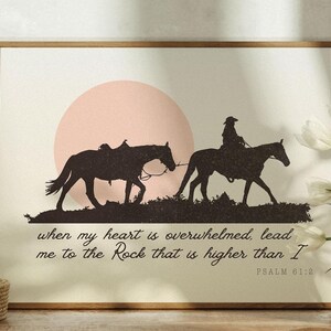 May include: A framed print with a silhouette of two horses and riders against a pink sunset. The text reads "when my heart is overwhelmed, lead me to the Rock that is higher than I" and "PSALM 61:2".