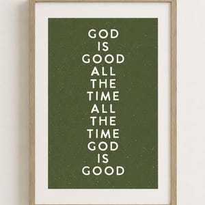 May include: A framed wall art print featuring a dark olive green background with white text that reads: GOD IS GOOD ALL THE TIME ALL THE TIME GOD IS GOOD. The print is enclosed in a light-toned wooden frame with a clean, rectangular profile.