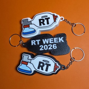 May include: Three keychains featuring a medical manual resuscitator design. Two are white with blue and red accents and the letters RT. One is black with the white text RT WEEK 2026. Each includes a silver metal split ring for attachment.