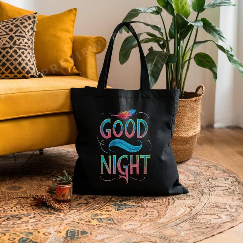 May include: A black tote bag with the words "GOOD NIGHT" in colorful, stylized lettering. The design includes a feather and flowing lines. The bag has two black handles and is sitting on a patterned rug.