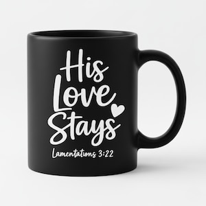 K&ouml;nnte beinhalten: Schwarze Keramik-Tasse mit wei&szlig;em Schriftzug "His Love Stays" und einem Herzsymbol. Der Text "Lamentations 3:22" ist darunter gedruckt. Die Tasse hat einen gebogenen Henkel.