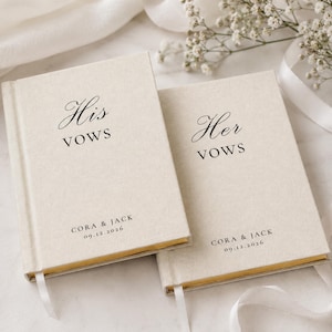 Può includere: Due libretti per i voti color crema con trama in lino e bordi delle pagine dorati. Il libretto a sinistra riporta il testo nero His VOWS, CORA & JACK, 09.12.2026. Il libretto a destra riporta il testo nero Her VOWS, CORA & JACK, 09.12.2026.