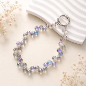 May include: A circular beaded accessory featuring iridescent, faceted glass beads that shimmer with blue, purple, and silver tones. The beads are strung together in a continuous loop and attached to a polished silver-toned metal spring ring clasp.