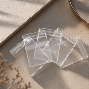 May include: Several clear, rectangular, resealable plastic pouches with a zip closure. The pouches are arranged on a neutral surface, with some overlapping. The transparent design allows visibility of the contents.