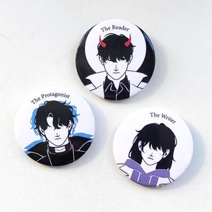 Può includere: Tre bottoni rotondi bianchi con illustrazioni di personaggi in stile anime in bianco e nero. Ogni bottone ha un titolo diverso: "The Reader", "The Protagonist" e "The Writer". Il Reader ha le corna rosse. Il Protagonist ha accenti blu.