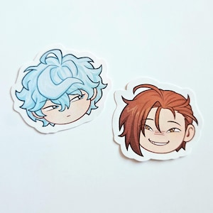 May include: Two die-cut vinyl stickers featuring stylized cartoon heads. One sticker shows a character with messy light blue hair and a neutral expression. The second sticker depicts a character with reddish-brown hair and a wide, toothy grin.