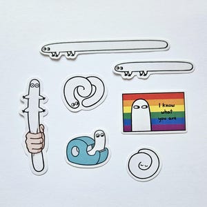 Può includere: Un set di otto adesivi di cartoni animati bianchi e neri con un fantasma, un verme, un dispenser di nastro adesivo e un arcobaleno. L'adesivo del fantasma ha il testo "So chi sei".