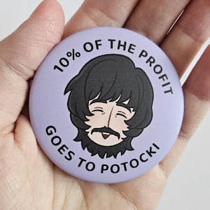 Puede incluir: Un botón redondo de color lila con el texto "10% OF THE PROFIT GOES TO POTOCKI" que rodea una ilustración de dibujos animados de un hombre con cabello negro y bigote. El hombre está sonriendo. El botón se sostiene en una mano.