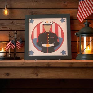 May include: A framed artwork depicting a military figure in a dark uniform, set against a red and white striped background with blue stars. The artwork is displayed on a wooden surface, with flags and a lantern nearby.