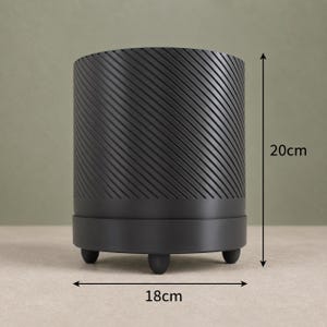 May include: A matte black cylindrical planter featuring a diagonal ribbed texture on the upper body, a smooth base, and three small rounded feet. The planter measures 20 cm in height and 18 cm in width as indicated by the visible measurement arrows.