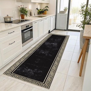 Puede incluir: Alfombra de pasillo negra y dorada con un patrón geométrico. La alfombra se coloca en una cocina con gabinetes blancos y un horno negro.