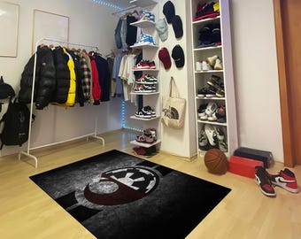 May include: A black and white rug with a red and white symbol in the center. The rug is in a room with a white shelf unit filled with shoes and hats.