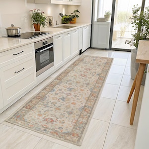 May include: A rectangular, beige runner rug with a floral pattern in shades of red, blue, and orange. The rug has a detailed border and is placed in a kitchen with white cabinets and appliances. The rug measures approximately 244 cm long.