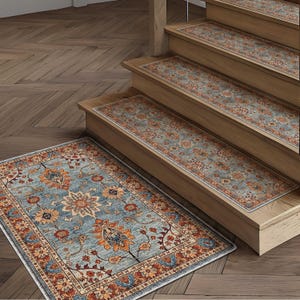 May include: A blue and orange floral patterned rug and matching stair treads. The rug and treads have a distressed, vintage look. The rug is rectangular and sits on a wooden floor. The stair treads are placed on wooden stairs.