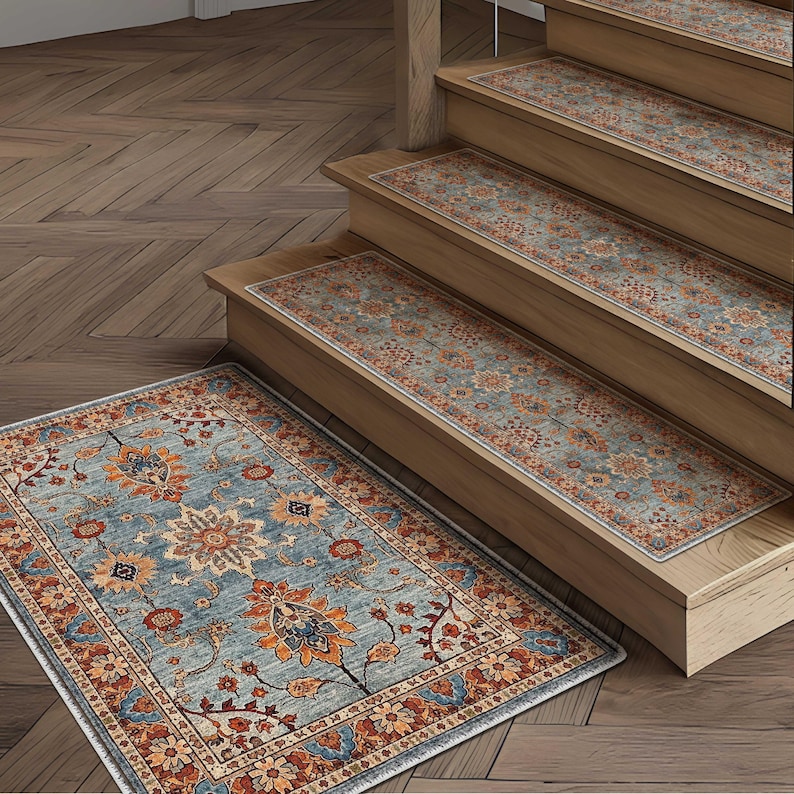 May include: A blue and orange floral patterned rug and matching stair treads. The rug and treads have a distressed, vintage look. The rug is rectangular and sits on a wooden floor. The stair treads are placed on wooden stairs.