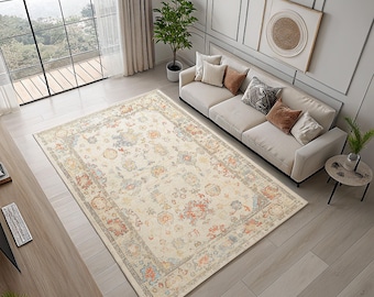 May include: A large, rectangular rug featuring a detailed floral design in cream, orange, blue, and grey hues. The rug is positioned in a living room, under a cream sofa and near a large window, creating a warm atmosphere.