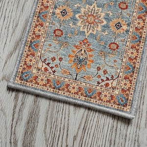 May include: A rectangular area rug with a detailed floral pattern in shades of blue, orange, and beige. The rug features a central medallion design and a decorative border. The rug is placed on a light-colored wooden floor.