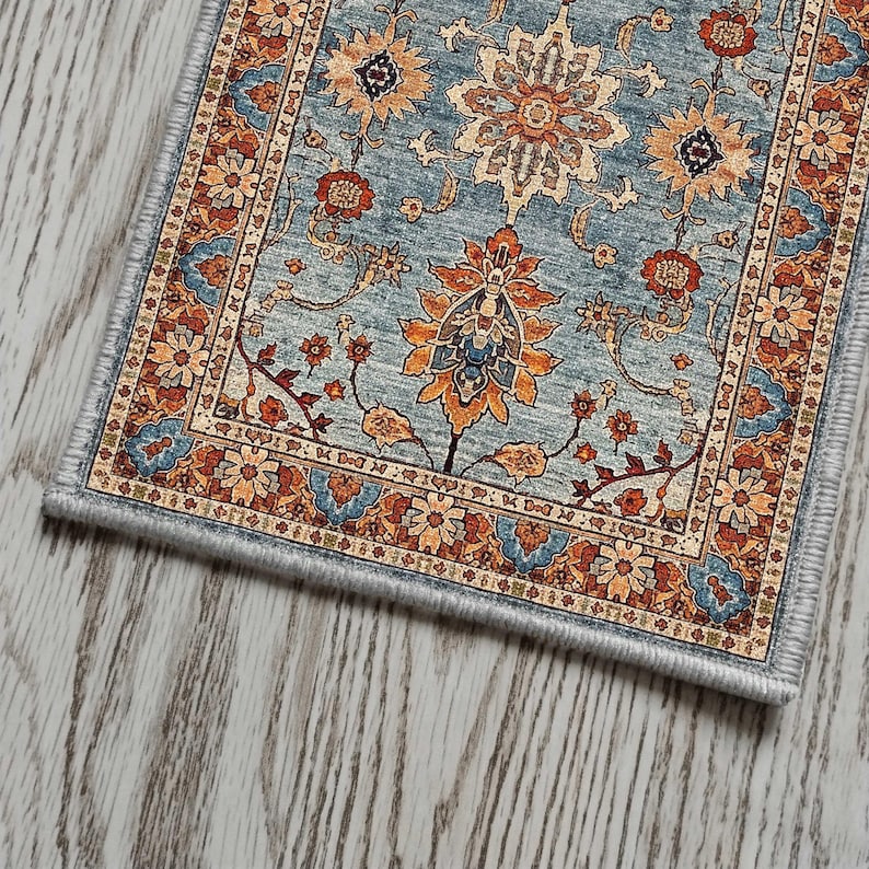May include: A rectangular area rug with a detailed floral pattern in shades of blue, orange, and beige. The rug features a central medallion design and a decorative border. The rug is placed on a light-colored wooden floor.