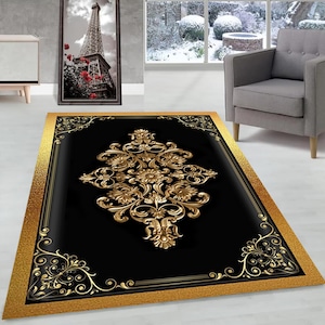 May include: A black and gold area rug with a large, ornate, gold floral design in the center. The rug has a gold border with a textured pattern.