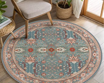 May include: A round area rug featuring a muted blue background with a symmetrical pattern of floral and geometric motifs in shades of cream, soft pink, and rust red, enclosed by a decorative border with repeating floral elements.