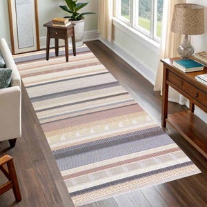 May include: A rectangular area rug with horizontal stripes in various neutral colors, including beige, gray, and brown. The rug has a textured appearance and is placed on a hardwood floor, adding warmth to the room's decor.