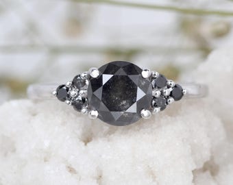 May include: A silver engagement ring with a large, round, black diamond surrounded by smaller black diamonds.