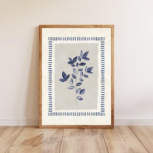 May include: A framed botanical print featuring a sprig of blue leaves against a light gray background. The artwork is bordered by a dashed blue line on a cream-colored background, encased in a wooden frame. The print is displayed on a wooden floor.