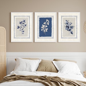 May include: Three framed botanical prints. Each print features a different floral arrangement in shades of blue and white against a neutral background. The frames are white with a blue striped border, creating a cohesive set for wall decor.