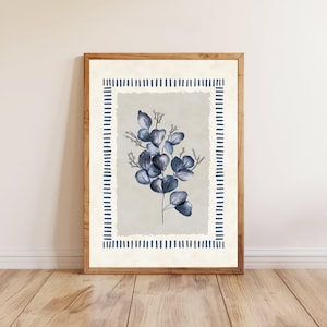 May include: A framed botanical print featuring a watercolor illustration of blue eucalyptus leaves and branches. The artwork is set against a light gray background with a decorative blue border. The frame is made of natural wood.