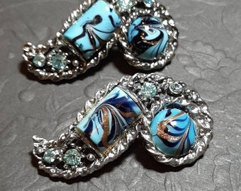 May include: A pair of silver tone earrings with blue and gold swirl designs. The earrings are shaped like a paisley pattern and have rhinestones.