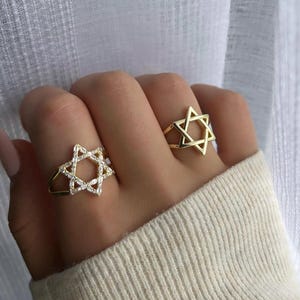 May include: Two gold rings with a Star of David design. One ring is set with clear cubic zirconia stones.