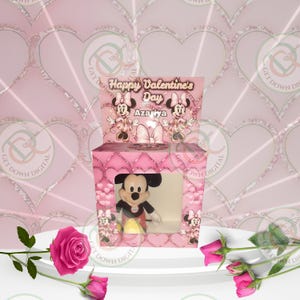 May include: Pink gift box with a clear window showing a plush Mickey Mouse toy inside. The box has a pink and white heart pattern and says "Happy Valentine's Day Azariya" on the top.