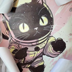 May include: A black cat wearing a pink and white astronaut suit with a black helmet. The cat is looking at the viewer and has a determined expression on its face. The background is a pink and white galaxy.