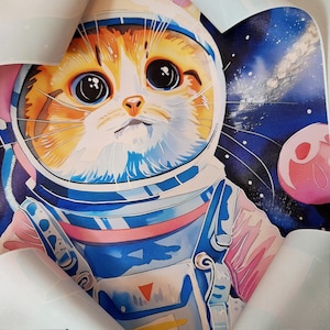 May include: A cartoon illustration of a cat wearing an astronaut suit with a blue and pink design. The cat is looking up with big, round eyes. The background is a dark blue space scene with stars and a pink planet.