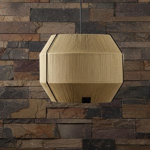 Può includere: Una lampada a sospensione a forma di tamburo con un esterno in filo o corda beige avvolto strettamente. Il paralume cilindrico è segmentato da sottili nervature metalliche verticali nere ed è sospeso da un singolo cavo nero centrale.