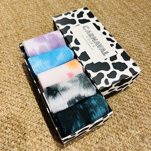 May include: A set of six colorful tie-dye socks in a black and white cow print box. The box has the text "CARNAVAL SOCKS" on the front.