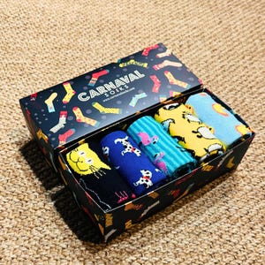 May include: A black box with a colourful pattern of socks on the lid. The box contains six pairs of colourful socks with various animal and geometric designs. The box is labelled "CARNAVAL SOCKS" and includes the website address "www.carnavalsocks.com".