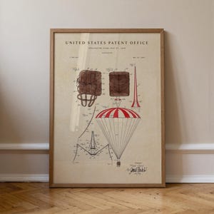 May include: A framed vintage patent illustration of a parachute design. The artwork features detailed diagrams in brown and red ink, with the text "United States Patent Office" at the top. The frame is made of light brown wood.