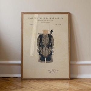 May include: A framed vintage patent illustration of a parachute harness. The diagram, labelled "United States Patent Office," features a detailed drawing of the harness in grey and black, with annotations. The frame is made of light brown wood.
