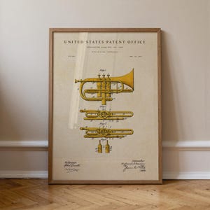 Op de afbeelding: Ingelijste vintage patentafdruk van een messing blaasinstrument. De afdruk toont gedetailleerde diagrammen van het instrument in gele en zwarte inkt, tegen een beige achtergrond. Het frame is gemaakt van lichtbruin hout.