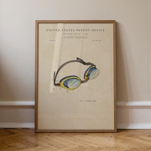 Peut inclure: Impression encadrée d'un brevet vintage de lunettes de natation. L'illustration, en jaune, bleu et noir, provient de l'United States Patent Office. L'impression est dans un cadre en bois et repose sur un sol en bois.
