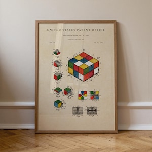 May include: A framed vintage patent illustration of a Rubik's Cube, with diagrams and a colourful cube. The print is in a wooden frame and is displayed against a neutral wall.