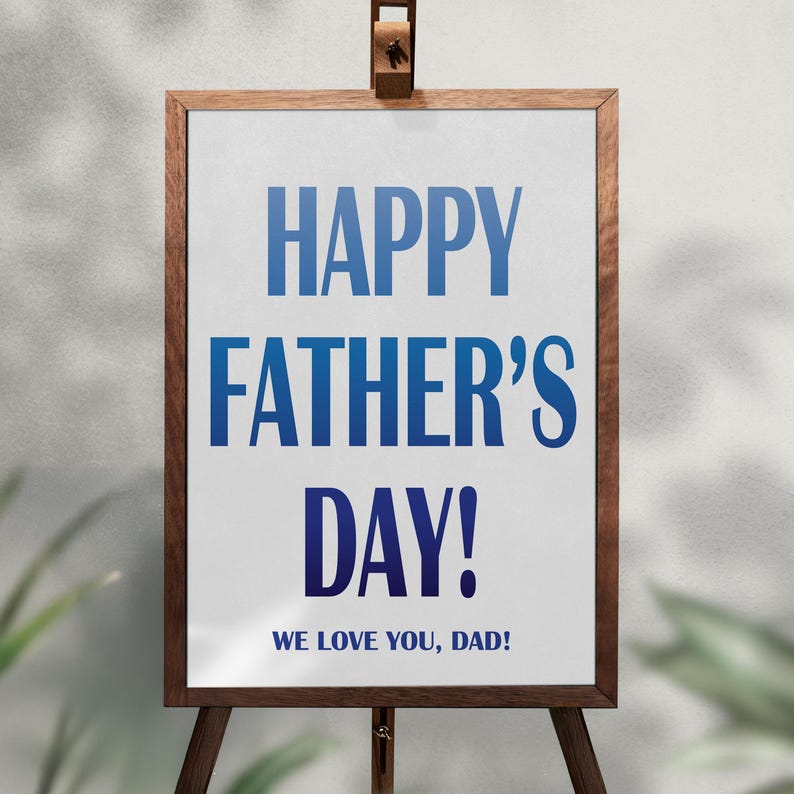 Op de afbeelding: Een houten ezel toont een wit bord met blauwe tekst met de tekst "HAPPY FATHER'S DAY!" en "WE LOVE YOU, DAD!". Het bord is omlijst in donker hout en staat tegen een neutrale achtergrond.