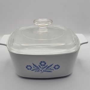 Puede incluir: Plato para hornear cuadrado blanco con tapa de vidrio y diseño floral azul. El diseño presenta tres flores azules con hojas verdes.